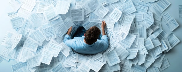 Stack of paperwork and compliance documents on a desk representing the need for organized IT documentation