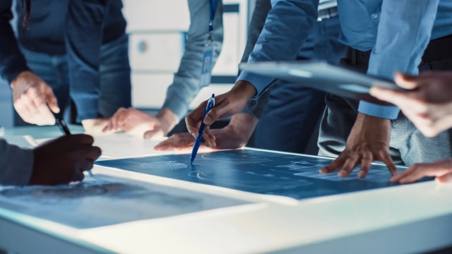 A cross-functional team collaborating around a digital display, bridging creative and technical disciplines